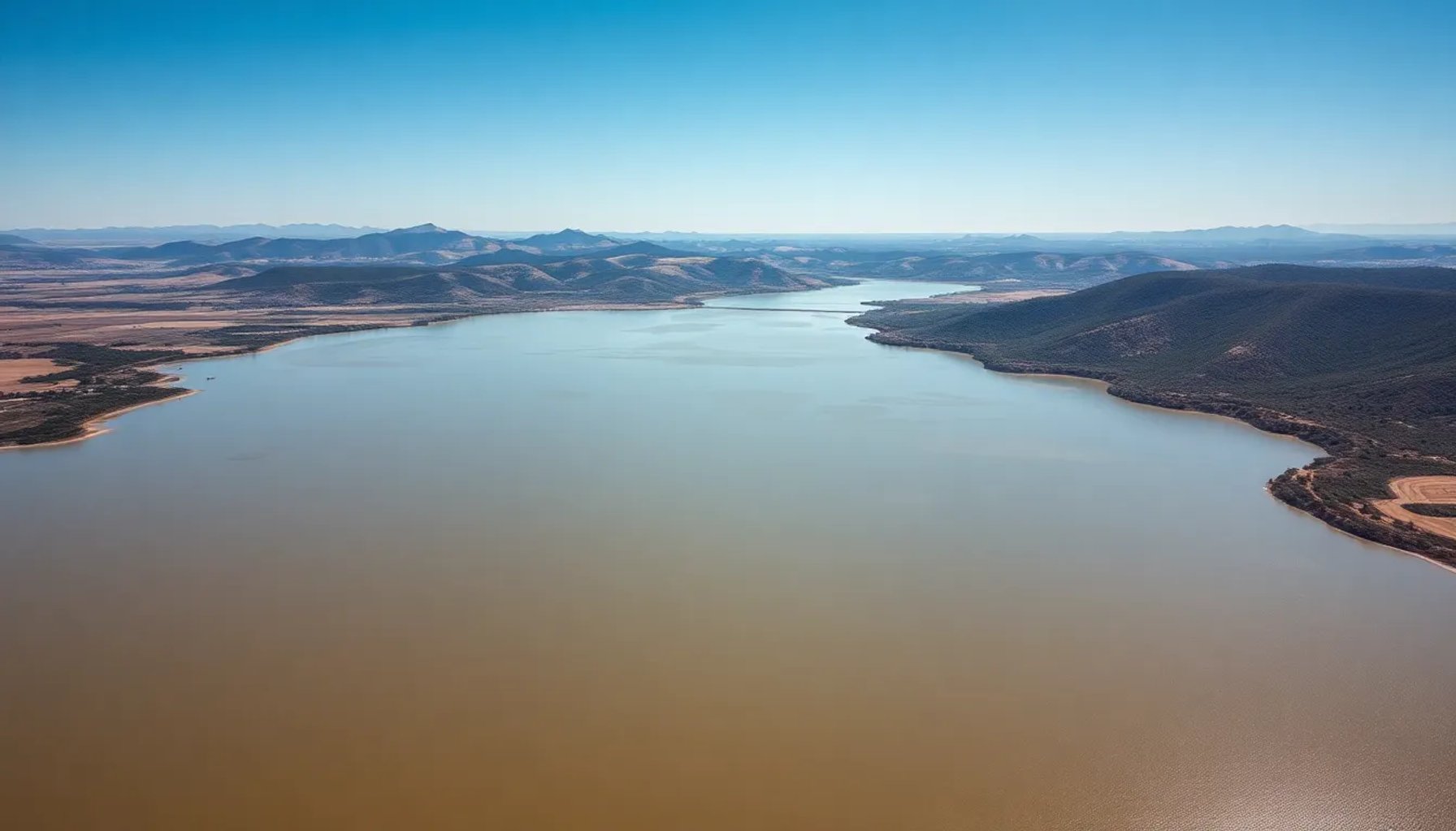 Vista aérea de la presa de Alcolea con aguas turbias y entorno agrícola